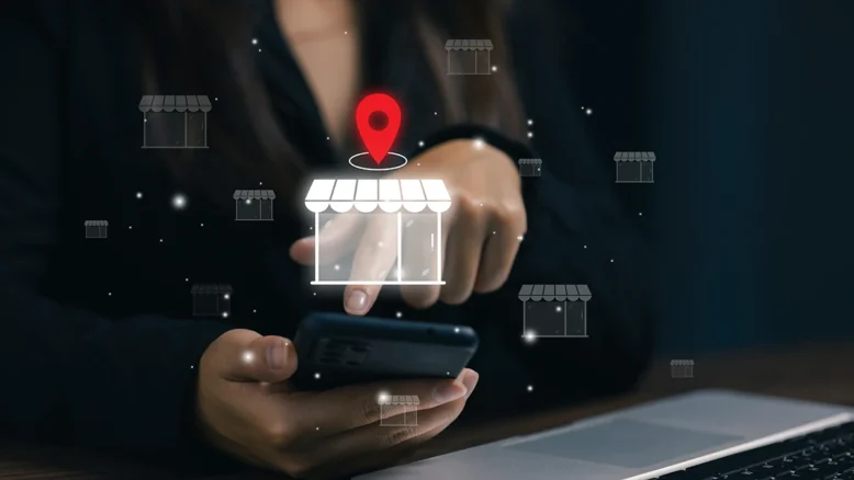 Woman typing on a smart phone and a local map pin and stand local business icon overlayed over hands.
